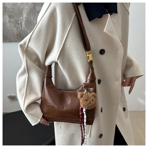 Detail of brown leather tote featuring Maison embossed logo and plush bear charm decor