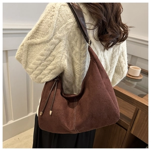 Détail d'un sac hobo en daim marron foncé avec surpiqûres blanches et glands latéraux