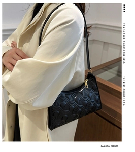 Detail of black underarm bag with embossed pattern and golden zipper on white coat