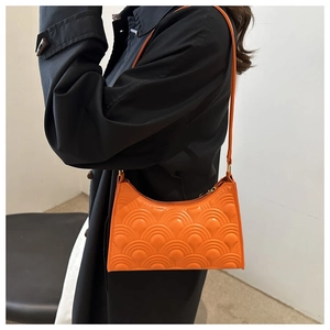 Detailed view of bright orange shoulder bag featuring scale texture and gold metal buckle