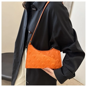 Macro view of bright orange quilted underarm bag with unique curved wave pattern