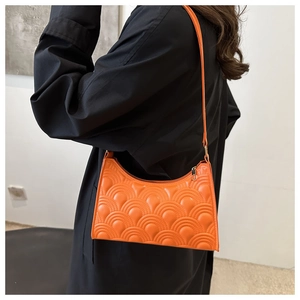 Detail of orange quilted underarm bag with wave texture worn over a black coat