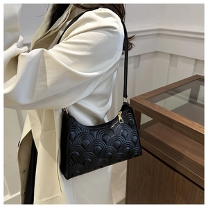 Detail of black underarm bag with wave embossed texture and gold zipper worn by model