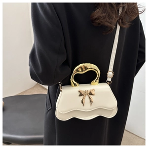 Detail of cream crossbody bag with gold metal handle and bow accent on a model