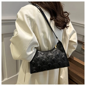 Detail of black quilted underarm bag with gold zipper shown on a beige blazer