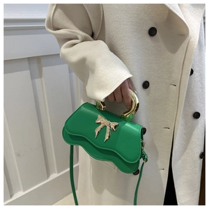 Detail view of a green bow-knot handbag with gold handle and wavy edges for women