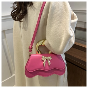Detail of pink shoulder bag with wavy edges, gold bow buckle and metallic handle