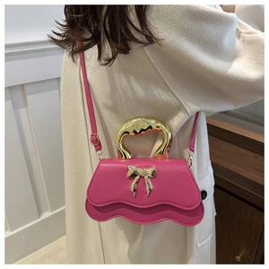 Detail of rose pink handbag with gold circular handle and bow accent on white coat