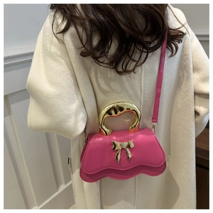 Close-up of a pink mini crossbody bag with gold bow detail and metallic handle on a model