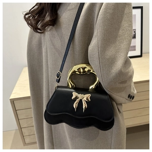 Detail of black crossbody bag with gold bow ornament and arc metal handle on model