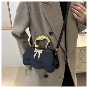 Close-up of black crossbody bag with gold bow ornament and chunky metal handle