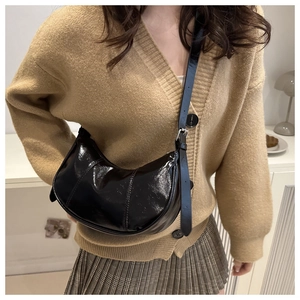 Detail of black glossy patent leather crescent bag worn by model in casual interior