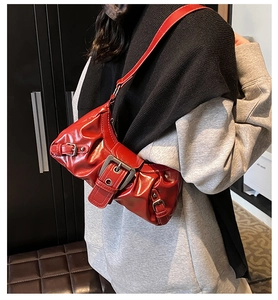 Close-up of a red patent leather underarm bag with pleated edges and silver belt buckle