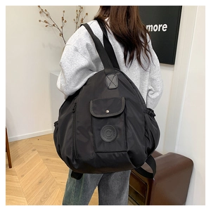 Rear view of model wearing a lightweight black nylon backpack with multi-pocket design
