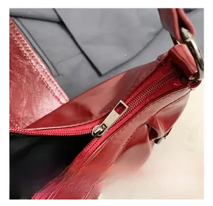 Macro shot of silver metal zipper detail on glossy deep red leather shoulder bag