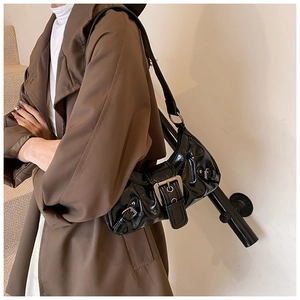 Detail of black glossy patent leather shoulder bag with vintage buckles and pleats