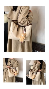 Detail view of large cream tote bag with brown straps and cute plush bear charm