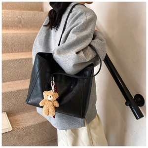 Detail of a black matte leather tote bag with a brown teddy bear charm on shoulder