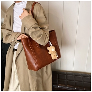 Detail of a large brown leather tote bag with a plush bear charm on a female model