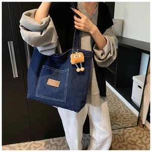 Close-up of denim tote bag with leather logo patch and cute plush toast charm accessory