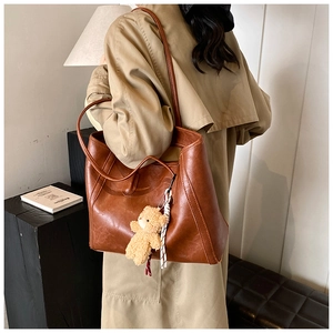 Detail of a large brown vintage tote bag with thin straps and a plush bear pendant accessory
