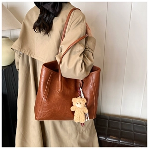 Brown leather tote bag with plush bear charm worn by a model in a minimalist setting