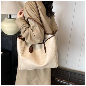 Close-up of a large beige tote bag with brown trim carried by a model in a trench coat