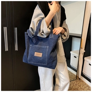 Detail of a large dark blue denim tote bag with a brown leather logo patch on front