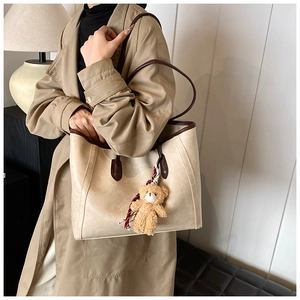 Detail of beige tote bag with brown handles and a cute teddy bear charm on windbreaker
