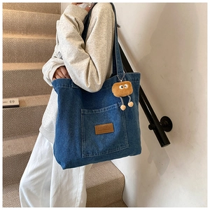 Detail der Denim-Einkaufstasche mit Außentasche, Lederetikett und Plüsch-Anhänger