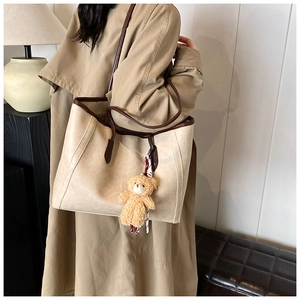 Close-up of large beige tote bag with brown trim and cute plush bear charm detail