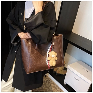 Detail of vintage dark brown faux leather tote bag with plush bear charm and woven rope