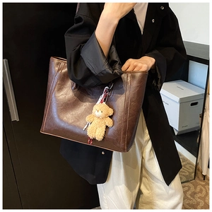 Detail of dark brown tote bag with oily leather texture and a plush bear charm