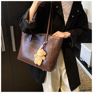 Detail of dark brown tote bag with glossy faux leather texture and a cute plush bear charm