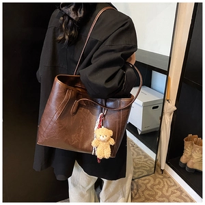 Detail of deep brown leather tote bag with plush bear charm and adjustable shoulder strap
