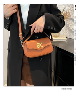 Detailansicht der braunen Ledertasche mit goldenem SK-Logo am Model mit dunklem Blazer
