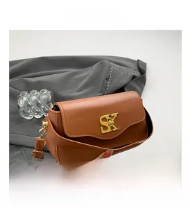 Detailansicht der braunen Kunstledertasche mit goldener SK-Schnalle auf grauem Mantel