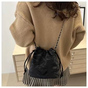 Detail of black drawstring bucket bag with textured pleats and metal chain shoulder strap