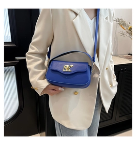 Detail der leuchtend blauen Umhängetasche mit goldenem SK-Logo und Perle auf elfenbeinfarbenem Blazer