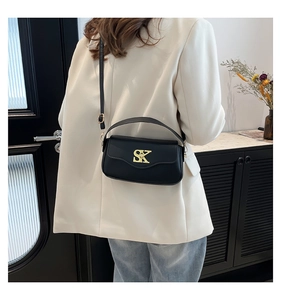 Detail der schwarzen Leder-Tasche mit großem goldnem SK-Metalllogo und schmalem Schultergurt