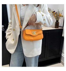 Detail einer leuchtend orangen Lederhandtasche mit Goldlogo an einem Model im Anzug