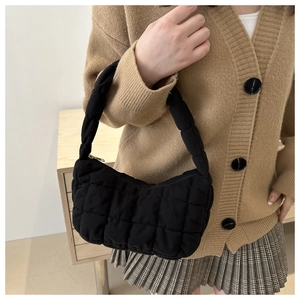 Détail du sac hobo matelassé noir avec texture cousue sur fond de tricot couleur camel