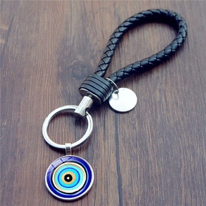 Braided leather evil eye keychain with blue glass charm and silver metal ring on wood