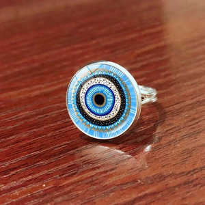 Macro shot of silver adjustable evil eye ring with blue concentric patterns on wood
