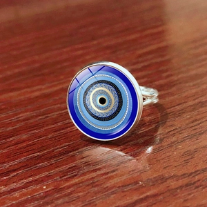 Macro shot of silver Evil Eye charm ring on a rustic reddish wood texture background