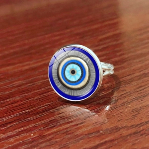 Macro shot of silver evil eye ring featuring a blue glass dome on a dark wood background