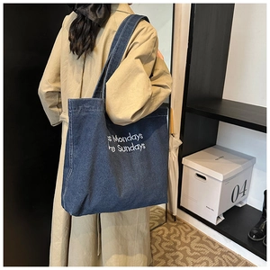 Detail of a dark blue denim tote bag with white lettering on a beige trench coat