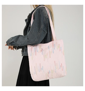 Detail view of pink canvas tote bag with multi-color wave embroidery on model's shoulder