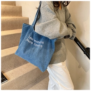 Detail of blue denim tote bag featuring 'Less Mondays More Sundays' white embroidery