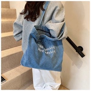 Detail of blue denim tote bag with Less Mondays white text slogan in lifestyle setting